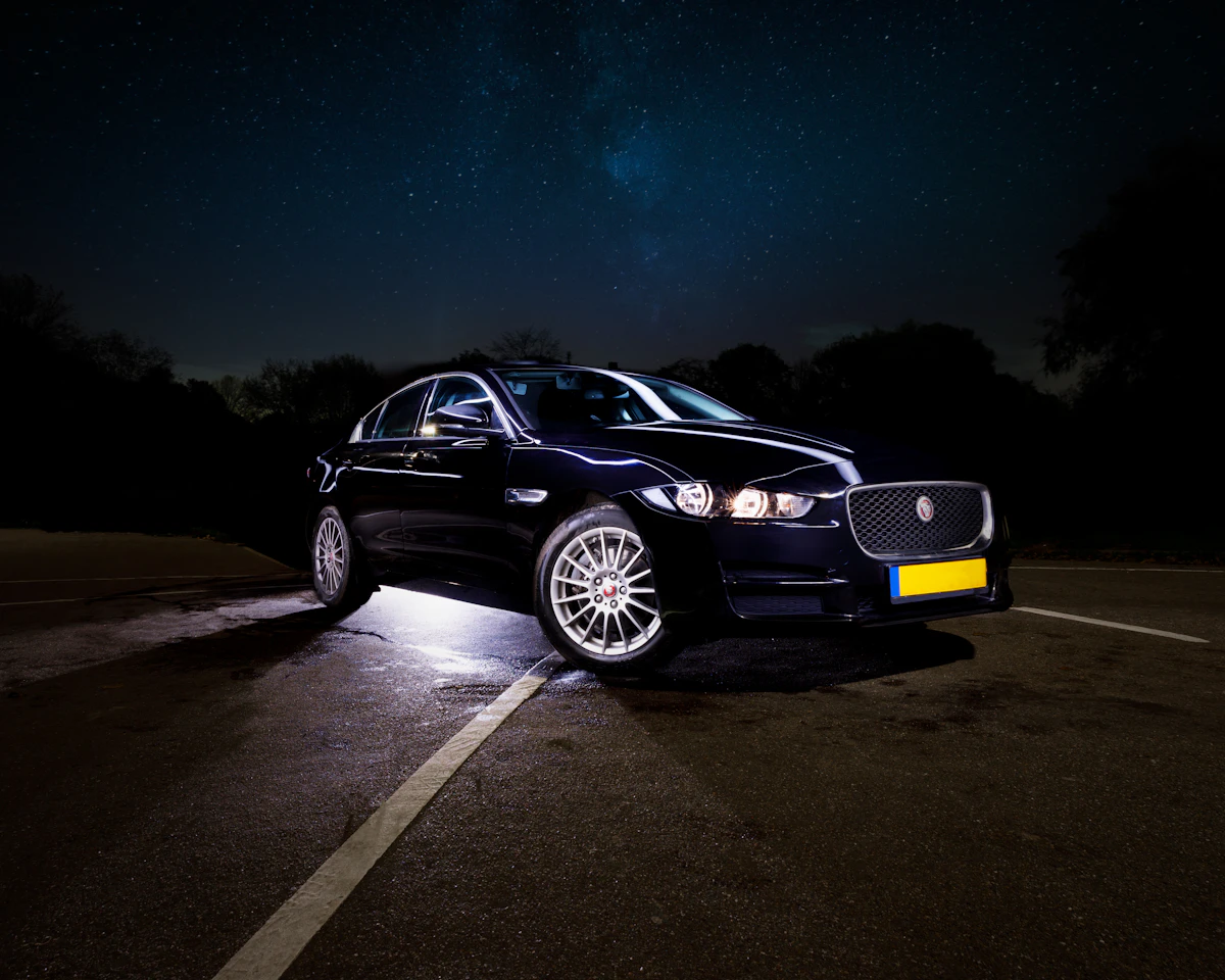 Berline noire de luxe garée de nuit sous un ciel étoilé, phares allumés, ambiance premium nocturne.