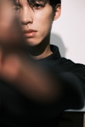 A close-up view of a person with short dark hair, capturing only part of their face sharply focused. The foreground is blurred, creating a depth effect, while the lighting highlights the facial features.