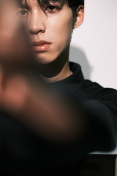 A close-up view of a person with short dark hair, capturing only part of their face sharply focused. The foreground is blurred, creating a depth effect, while the lighting highlights the facial features.