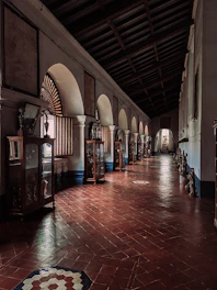 A warmly lit museum corridor with blue and white mosaic floors and traditional artworks displayed on the walls.