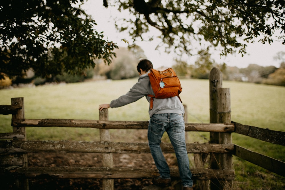 a man with a backpack leaning on a fence