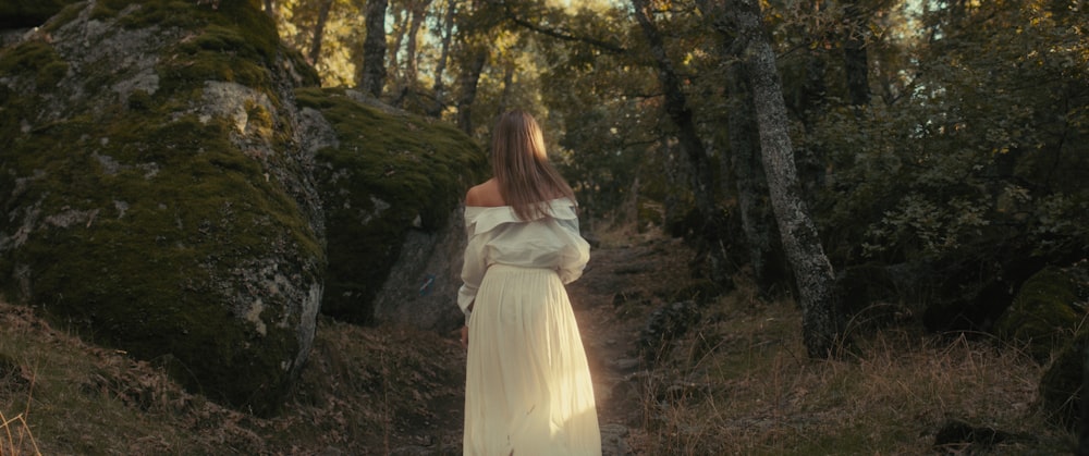 a woman in a white dress walking through a forest