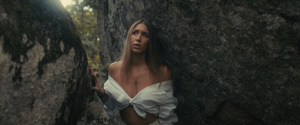 a woman in a white top is standing between two large rocks