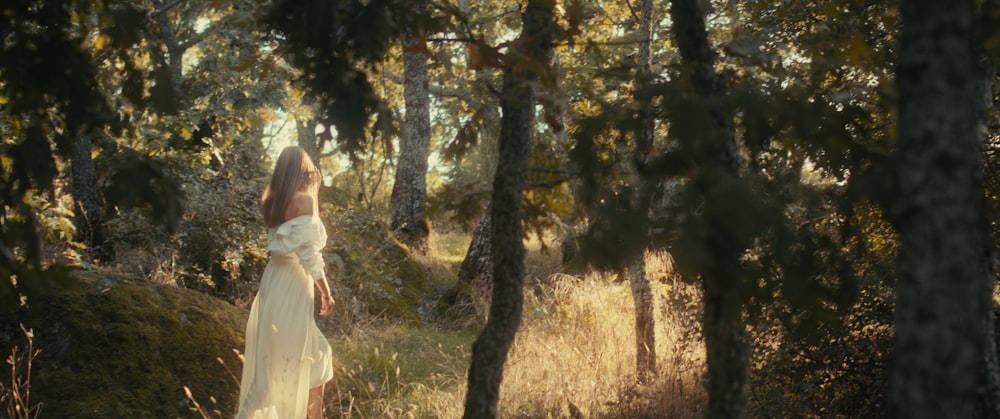 a woman in a white dress walking through a forest