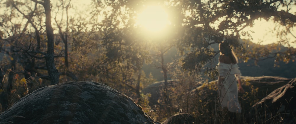 a woman in a white dress walking through a forest