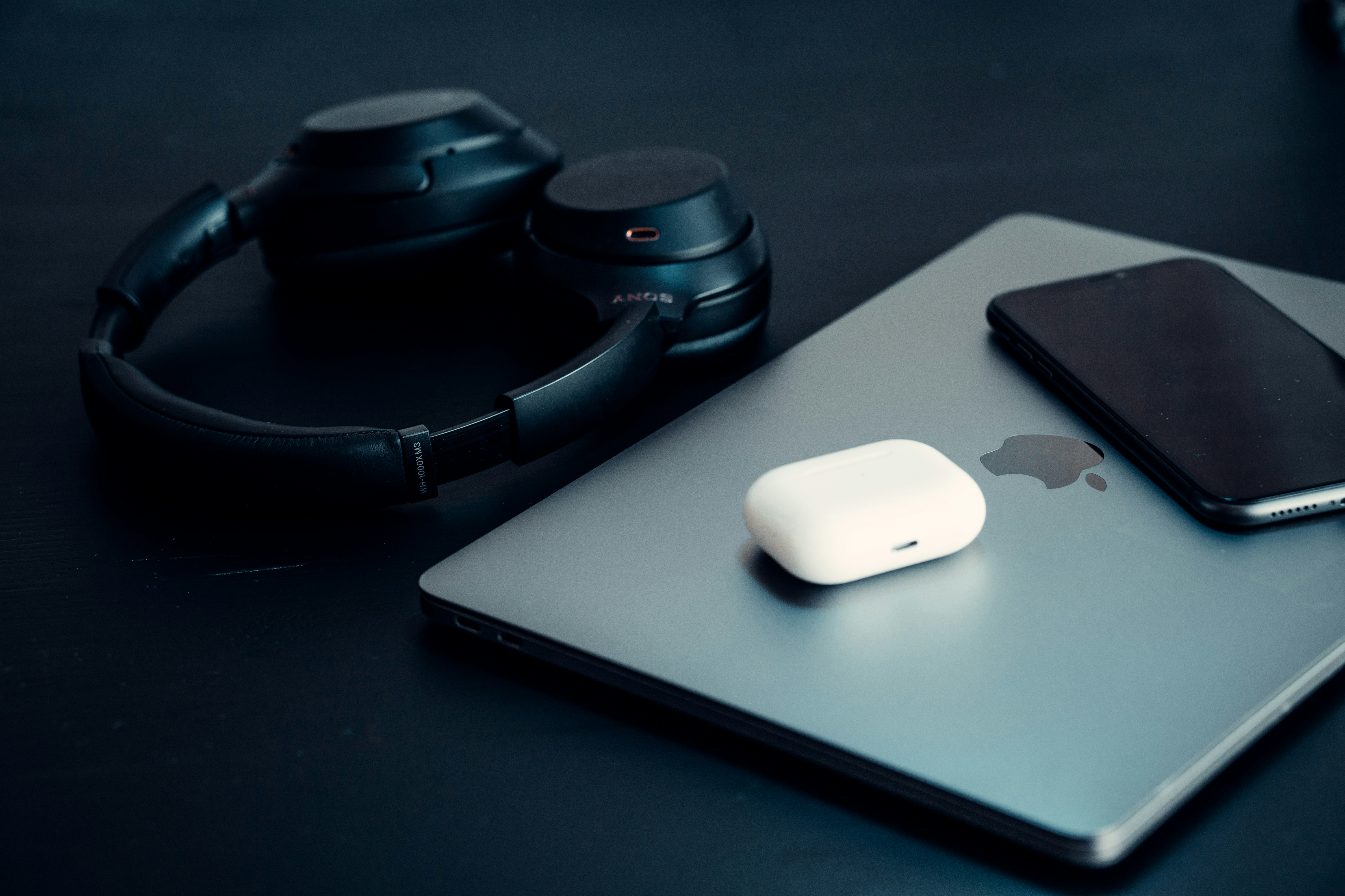 Various electronic gadgets including headphones, phone and laptop on dark background