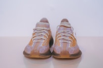 A pair of sneakers with a knitted upper design featuring shades of brown, beige, and lavender. The shoes have thick, ribbed outsoles and a lace-up style with chunky laces.