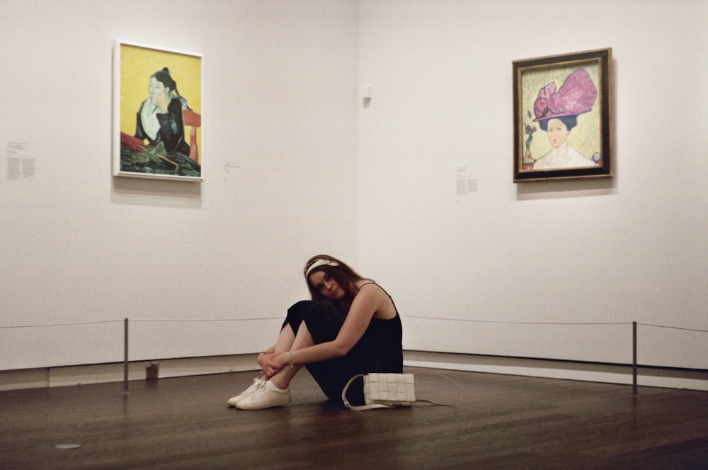 a woman sitting on the floor in front of paintings
