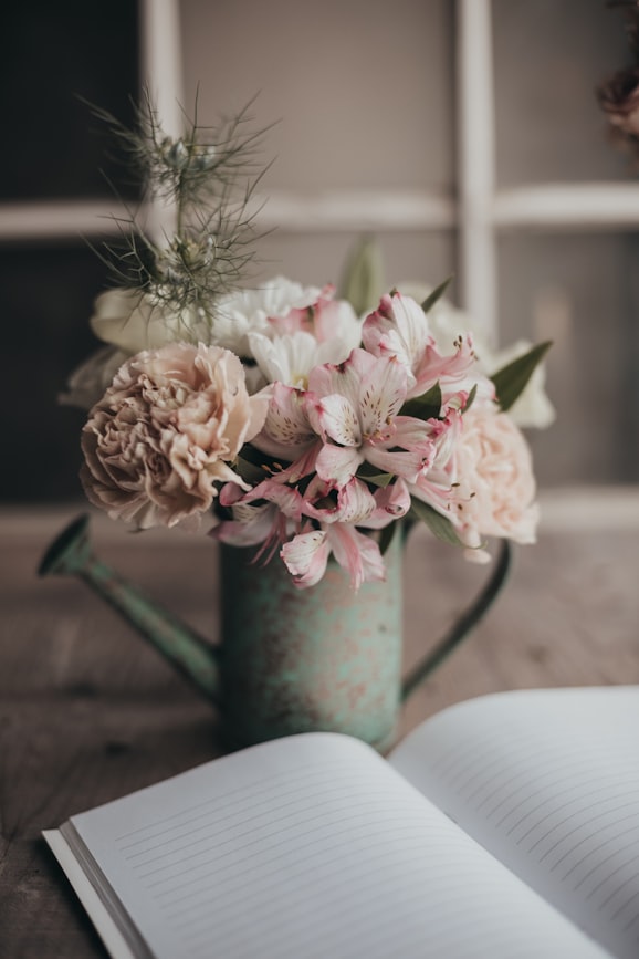 Gießkanne mit Blumen neben einem offenen Tagebuch – ein Gartentagebuch führen