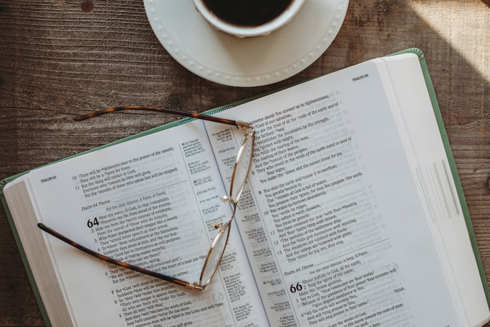 an open book with glasses on top of it next to a cup of coffee