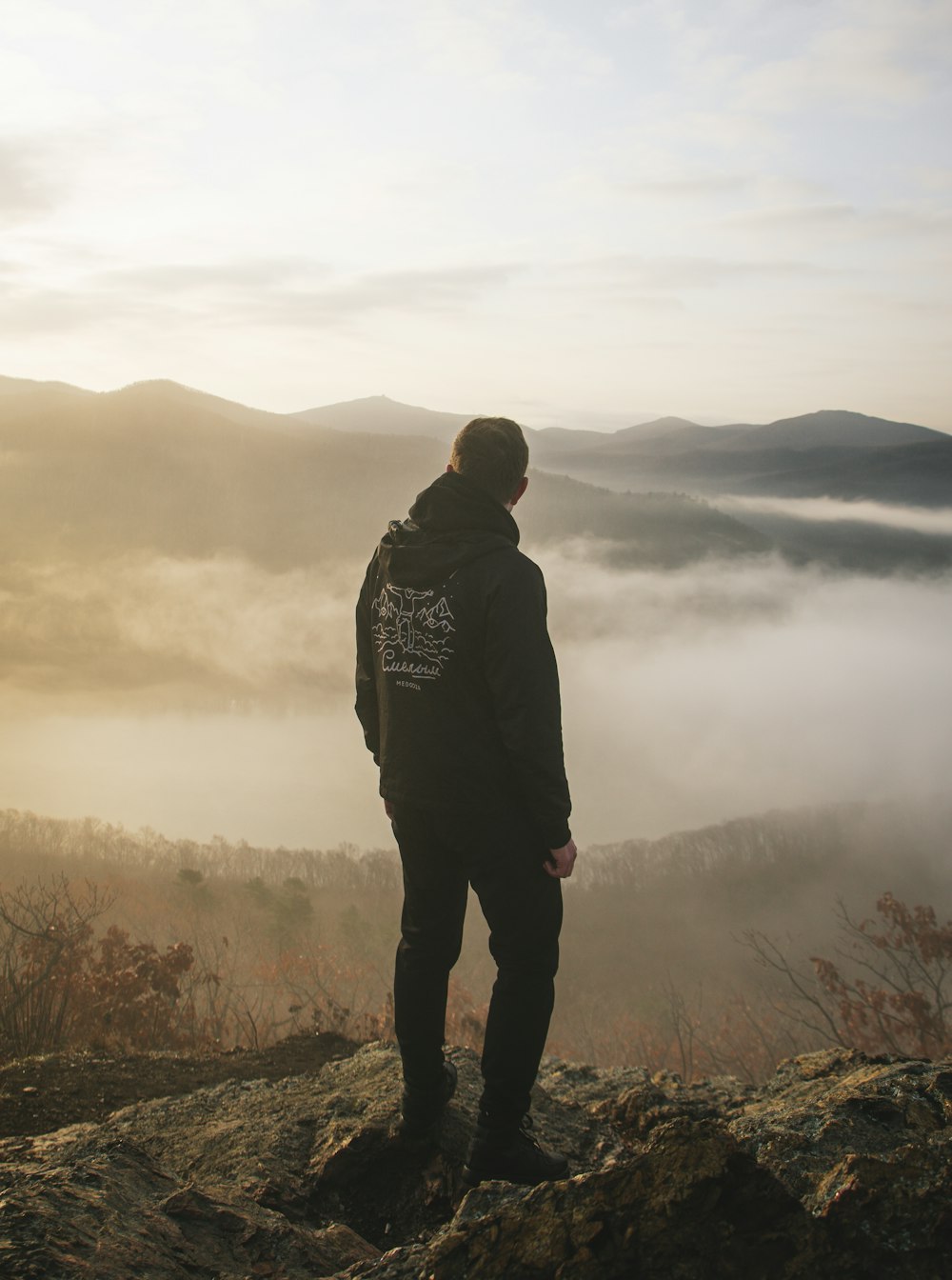 Un homme debout au sommet d’une montagne surplombant une vallée brumeuse
