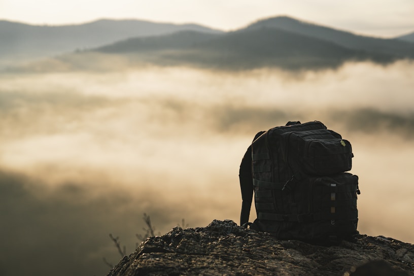 A rugged outdoor backpack resting on a rocky trail with a mountain backdrop at sunrise.