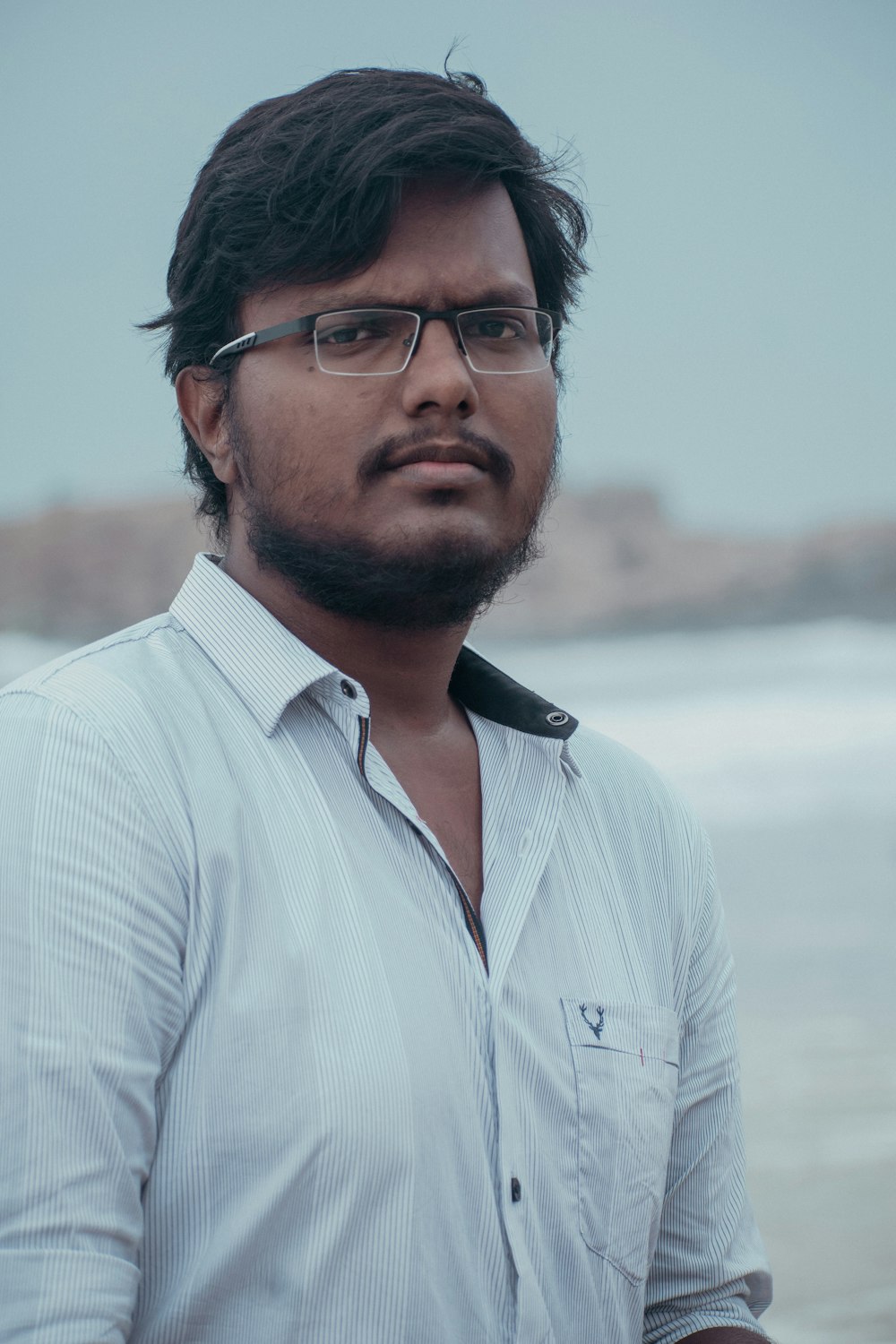 a man with glasses standing in front of a body of water