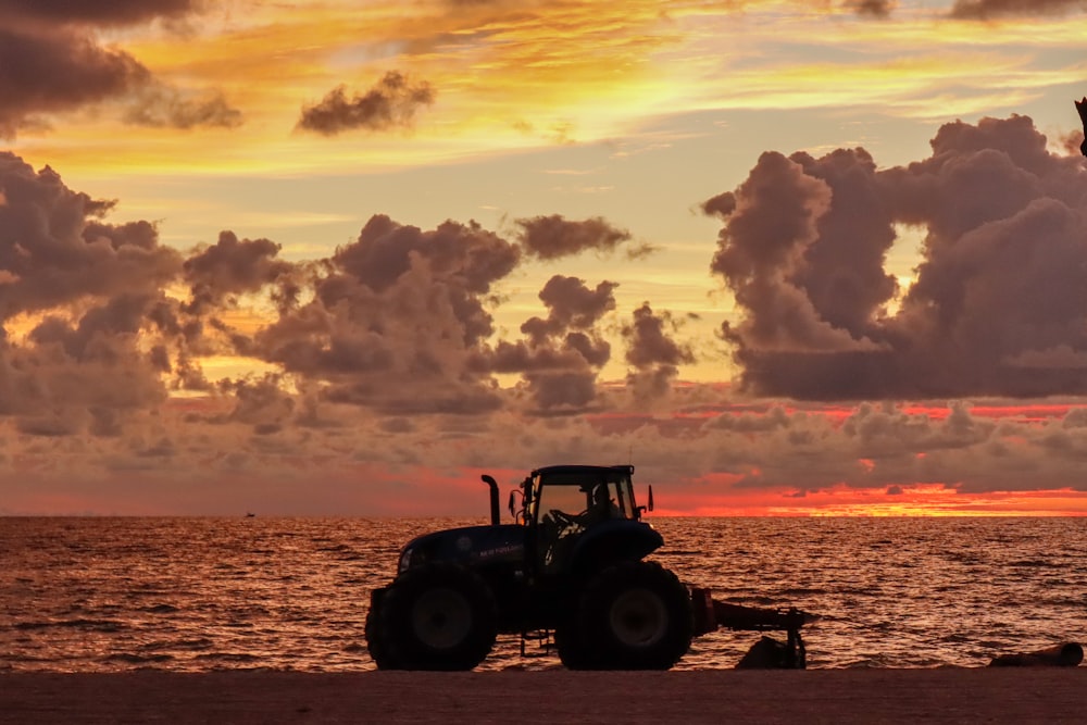 a tractor is parked on the beach as the sun sets