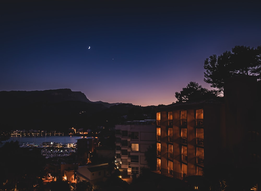 a night view of a city with a lake and mountains in the background