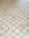 A wooden parquet floor is composed of square tiles arranged in a checkered pattern. The tiles vary slightly in color and grain, creating a natural and textured appearance.