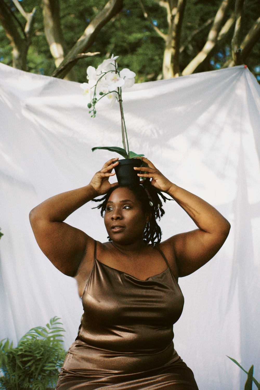 a woman in a brown dress holding a flower on her head