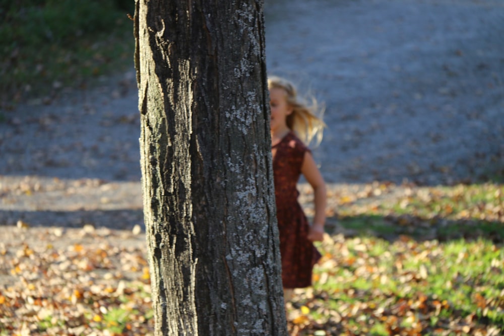 a little girl standing next to a tree