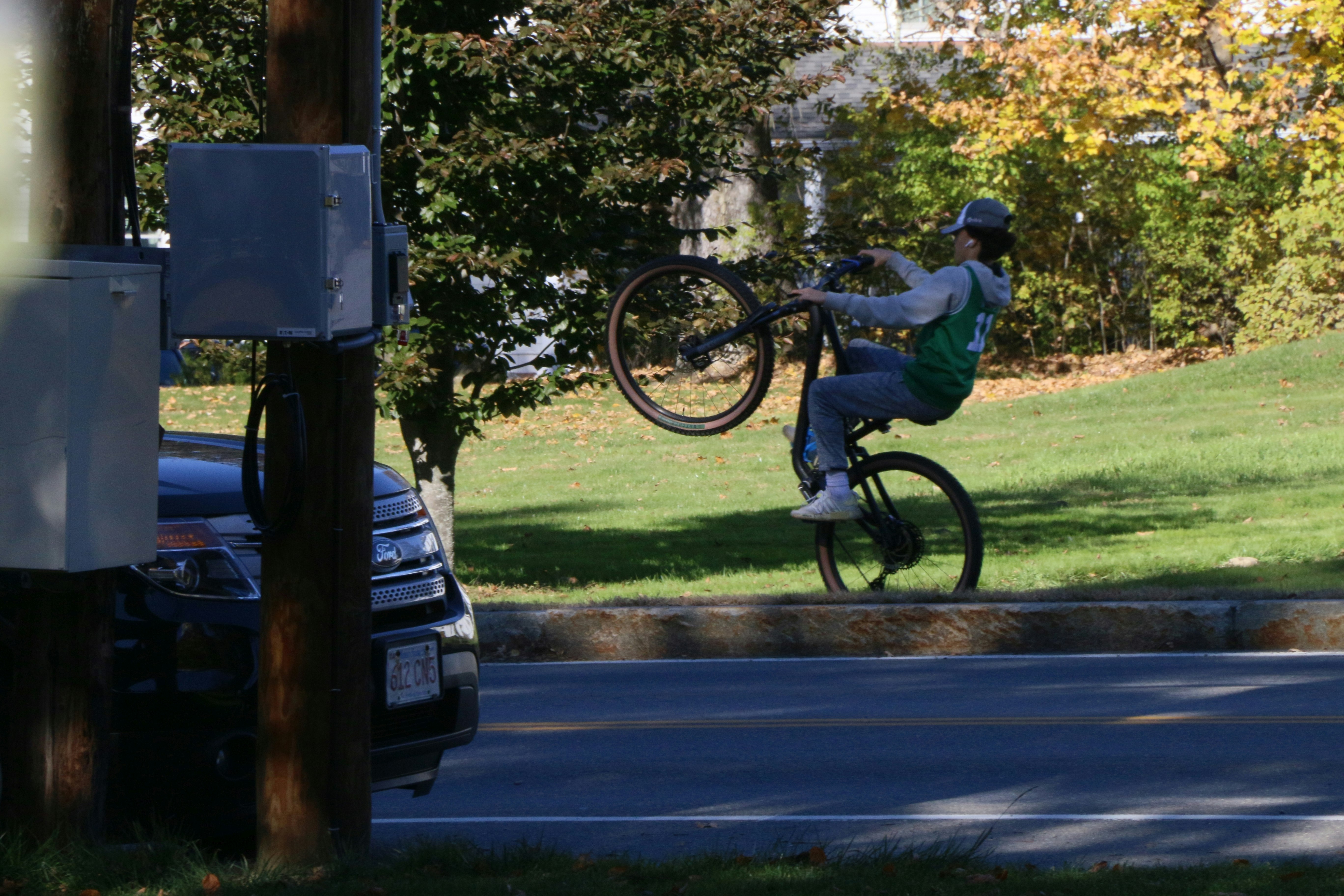Daredevil biking on sidewalk in Groton MA.  Front wheel up in the air.  Leaning back in the saddle.  
