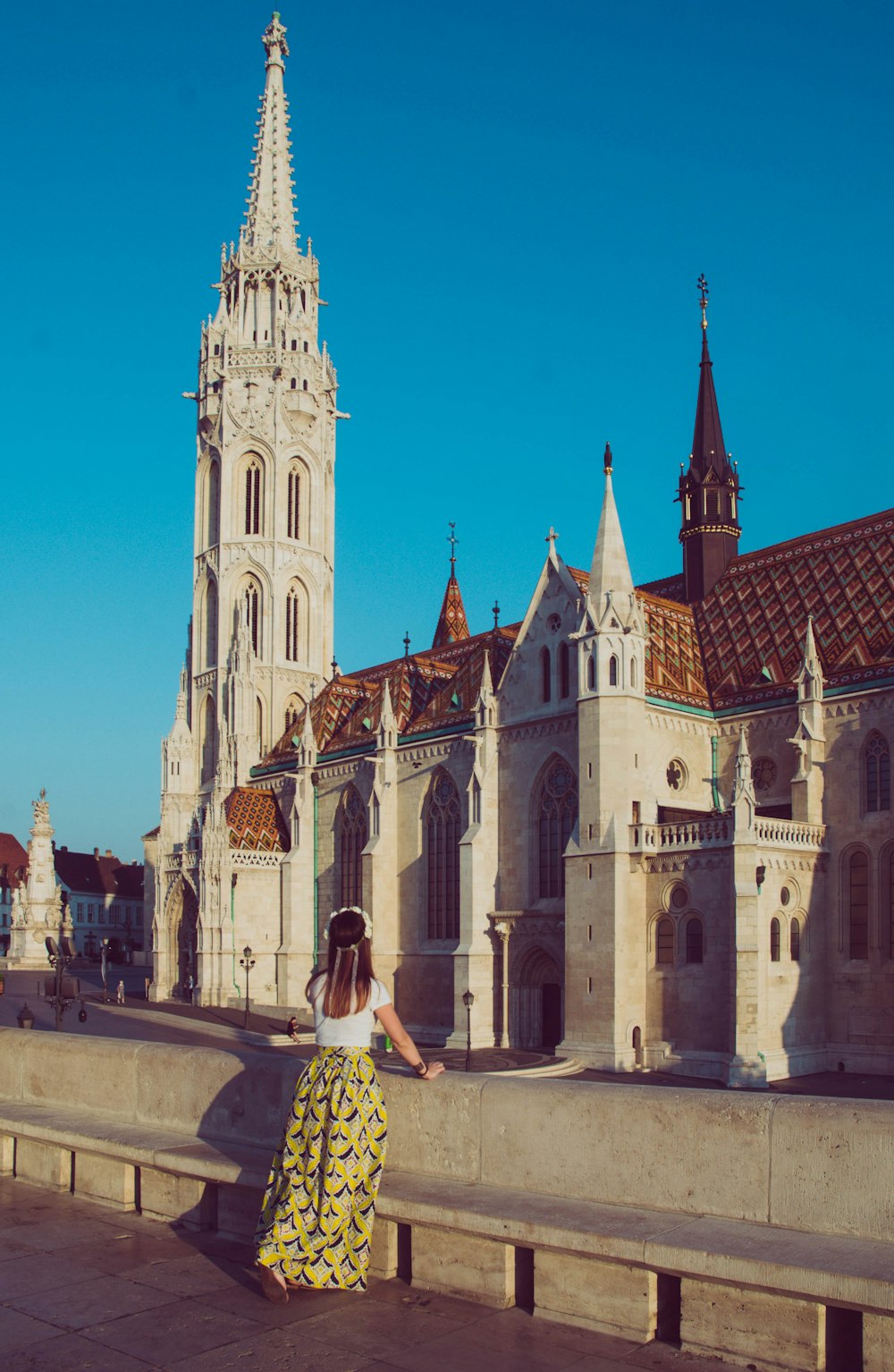 a woman in a yellow and white dress standing on a bridge in front of a