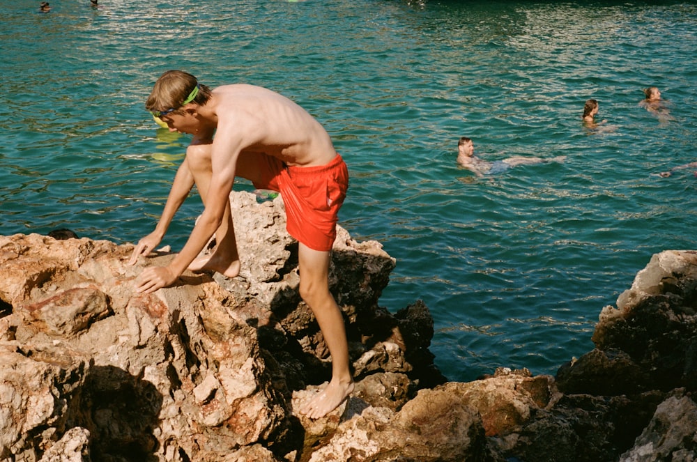 a man standing on top of a rock next to a body of water