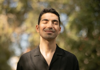 a man with his eyes closed standing in front of trees