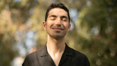 a man with his eyes closed standing in front of trees