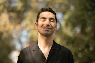 a man with his eyes closed standing in front of trees