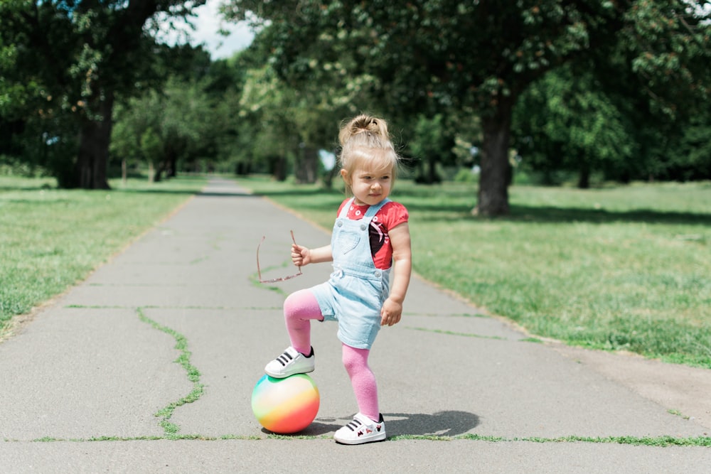 a little girl playing with a ball on a sidewalk