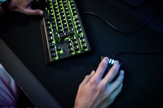 A close-up of hands on a keyboard and mouse with a glowing blue backlight, symbolizing tech and gaming.