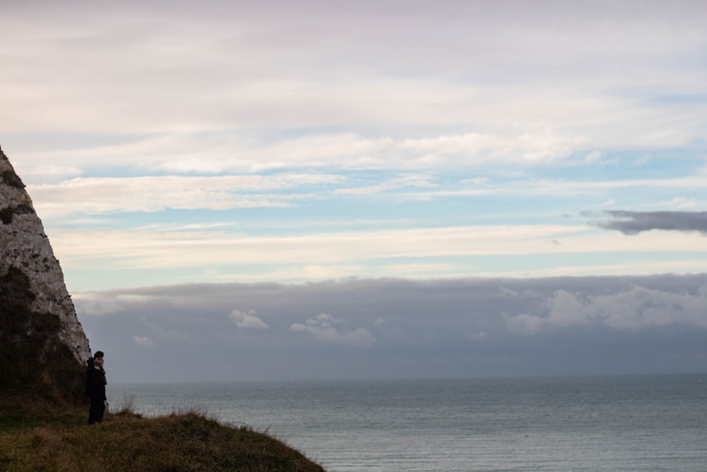 a man standing on top of a cliff next to the ocean