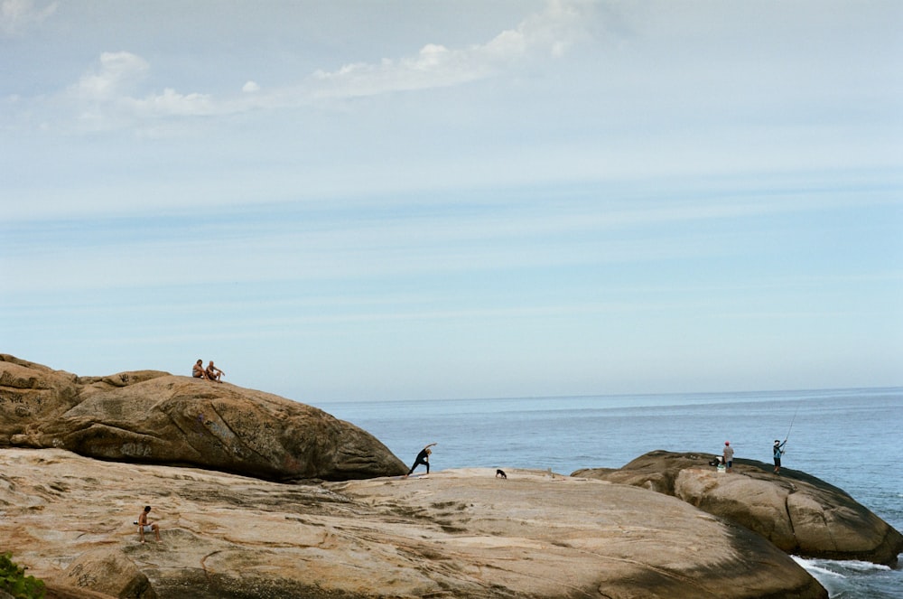 a group of people standing on top of a large rock next to the ocean