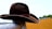 A close-up of a vintage leather cowboy hat resting on a wooden fence post at sunset.