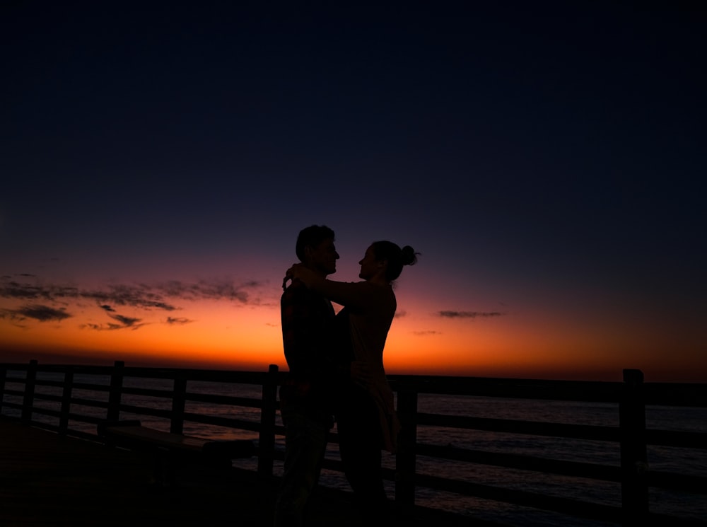 a couple standing next to each other at sunset