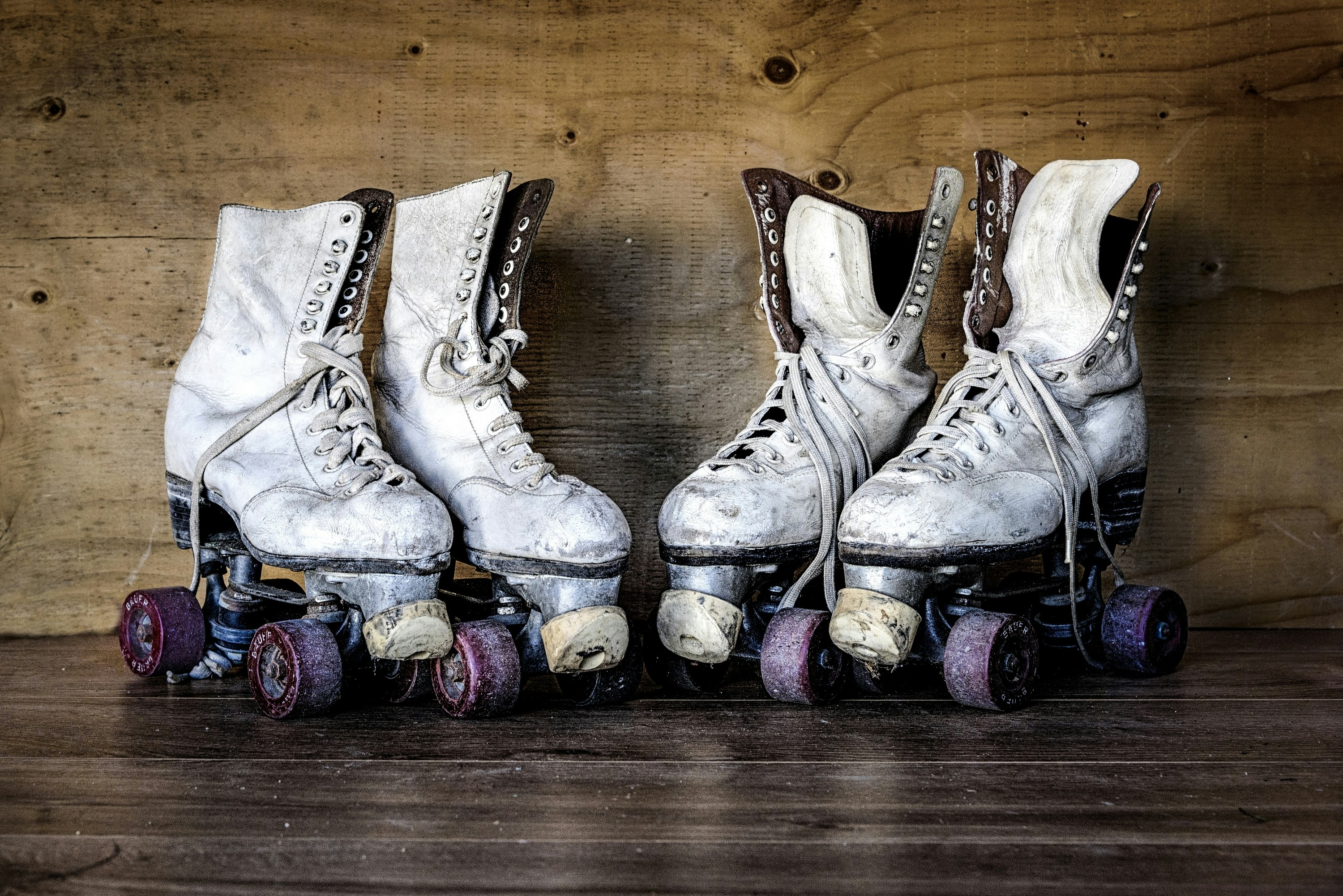 Two pairs of worn white quad skates standing on old wooden boards