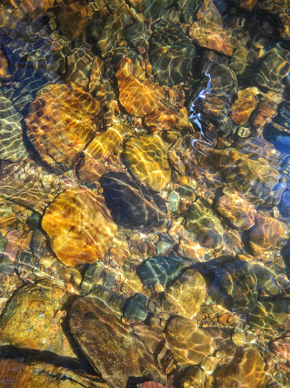 A close-up of cool, clear stream water moving over rounded rocks — the kind of brief, gentle rinse suited to a tumbled amethyst piece