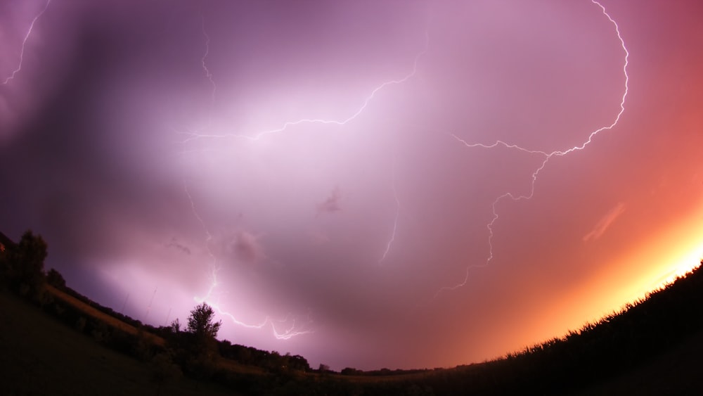 a purple and orange sky with a couple of lightnings