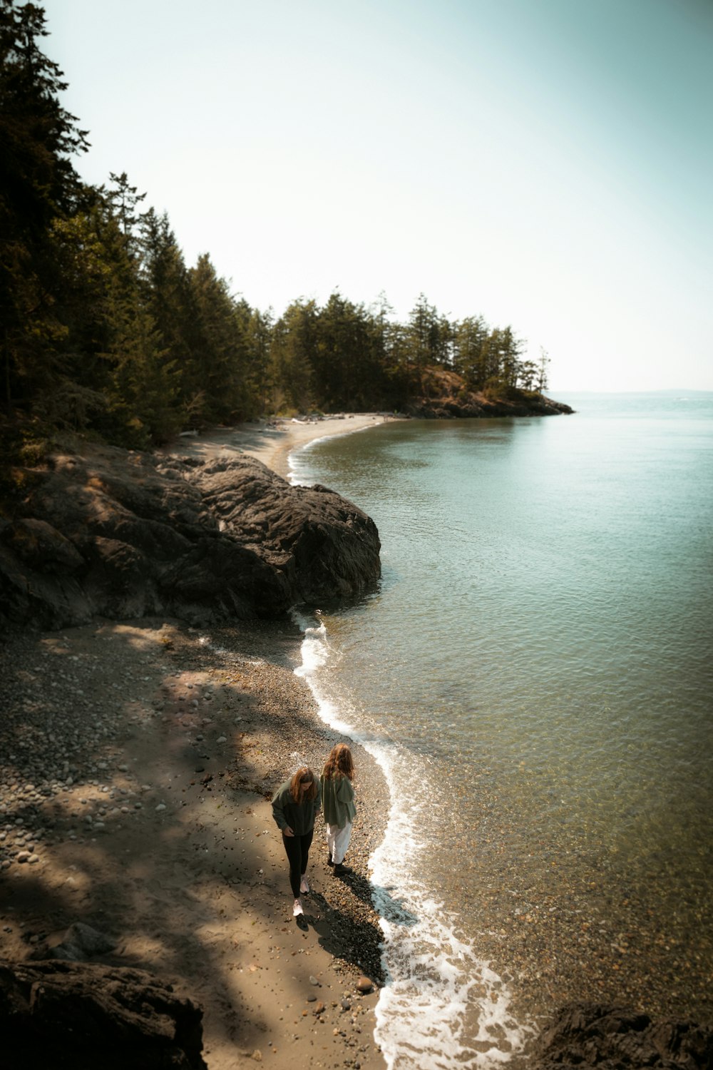 a couple of people walking along a beach next to the ocean