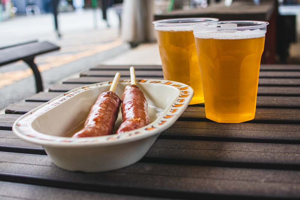 two glasses of beer and two hot dogs on a table