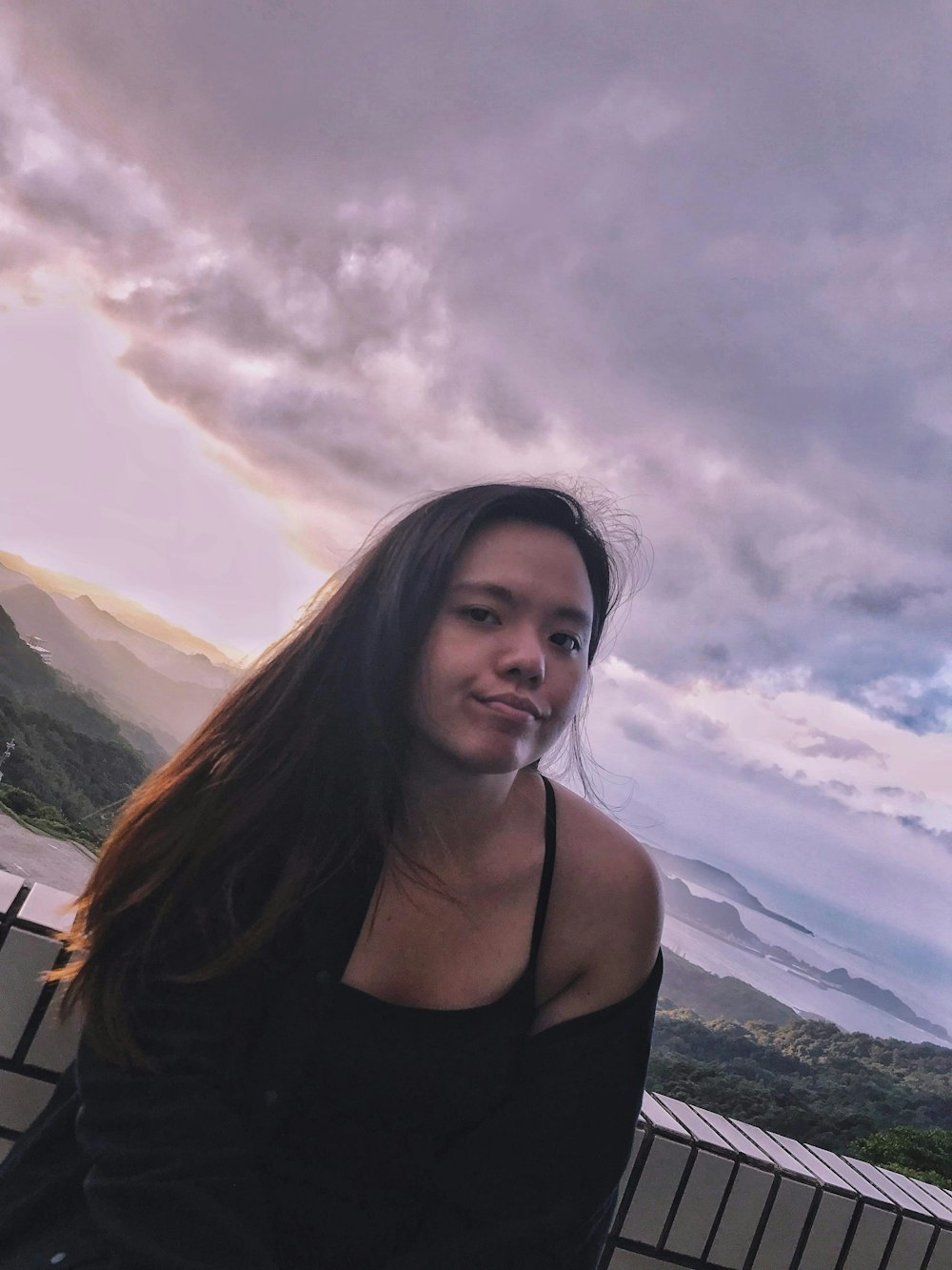 a woman standing in front of a fence under a cloudy sky