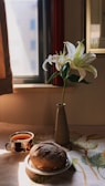 A gentle morning scene with a cup of herbal tea beside a blooming plant on a sunlit table.
