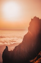 A dramatic cliff face bathed in the warm glow of sunset with clouds swirling below.