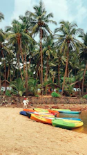 A cheerful group of friends preparing kayaks on the sandy shore with palm trees in the background.