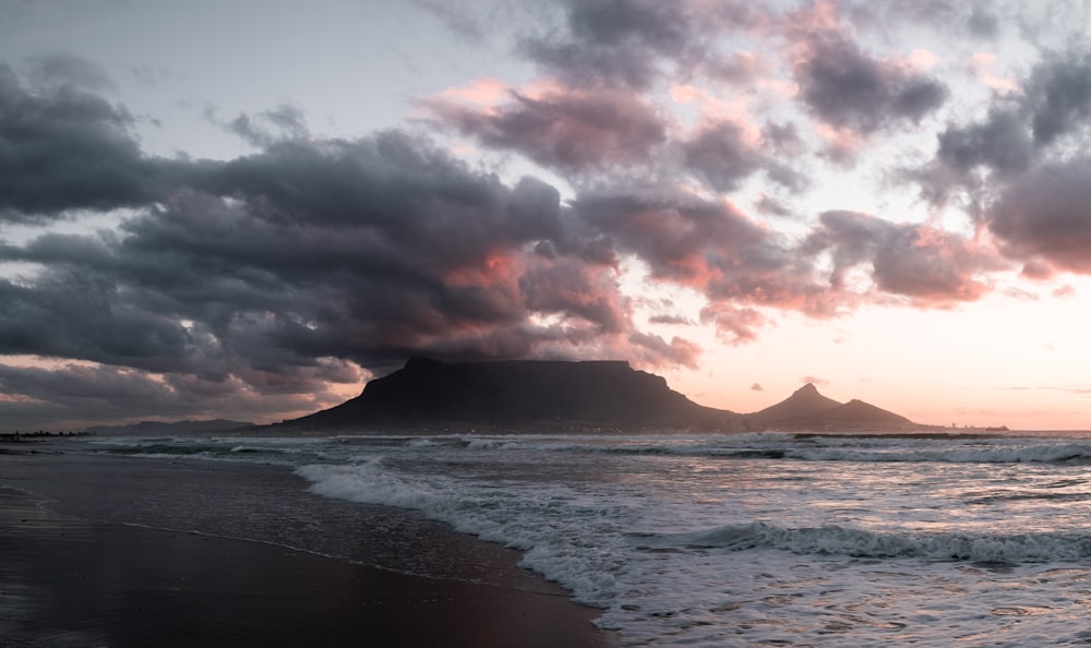 a beach with waves and a mountain in the background