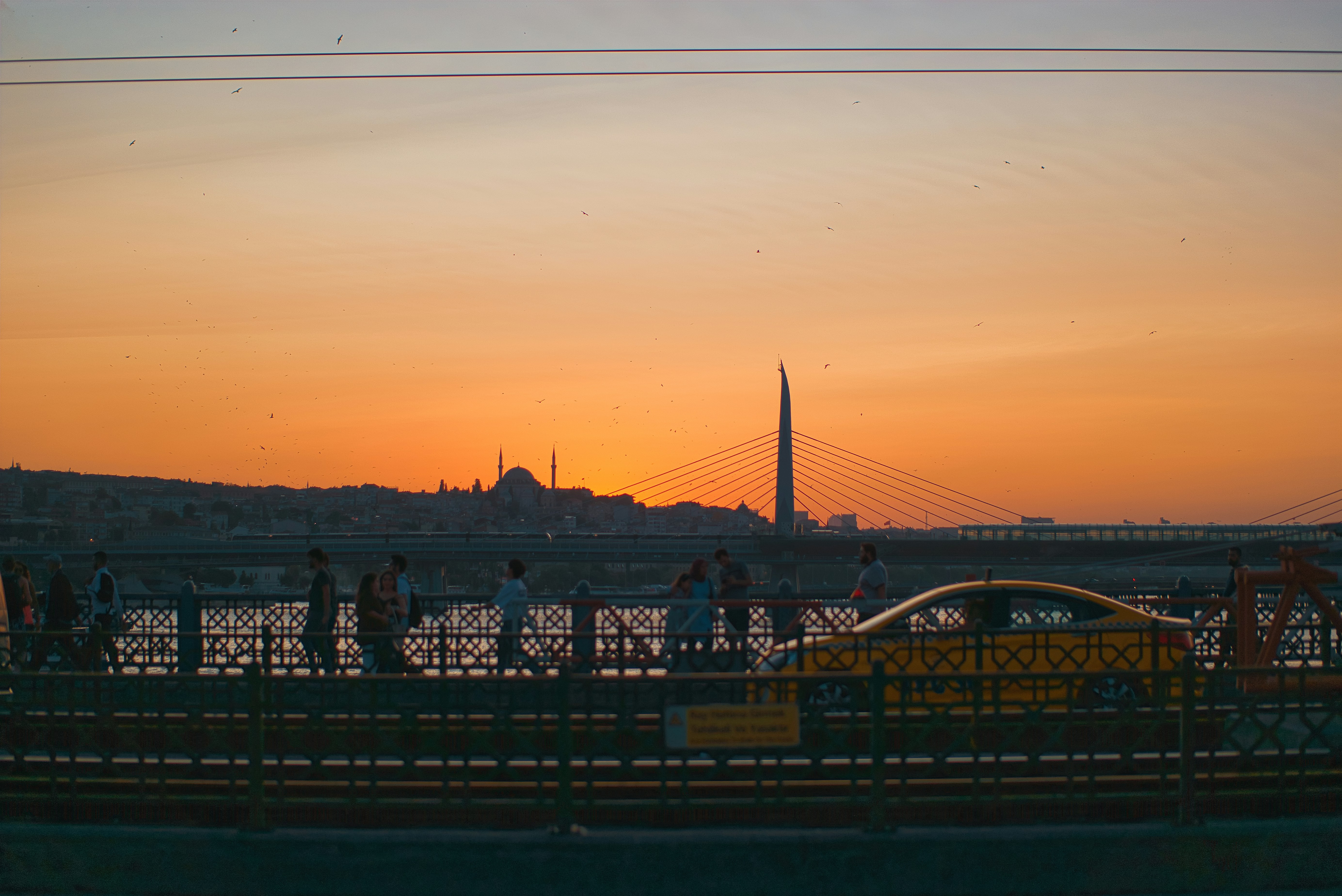a group of people walking across a bridge at sunset