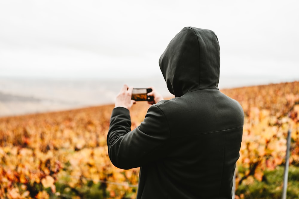 a man in a hoodie taking a picture of a vineyard