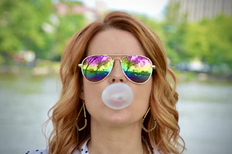 A fierce woman in a pink faux fur coat blowing a bubblegum bubble, with smeared red lipstick and leopard print background.