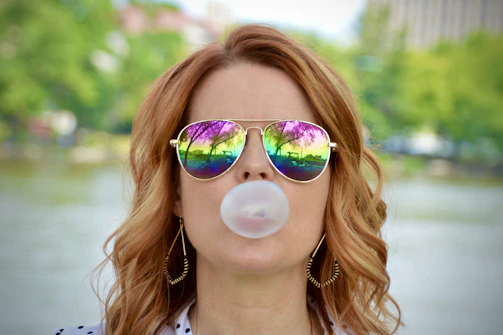 A fierce woman in a pink faux fur coat blowing a bubblegum bubble, with smeared red lipstick and leopard print background.