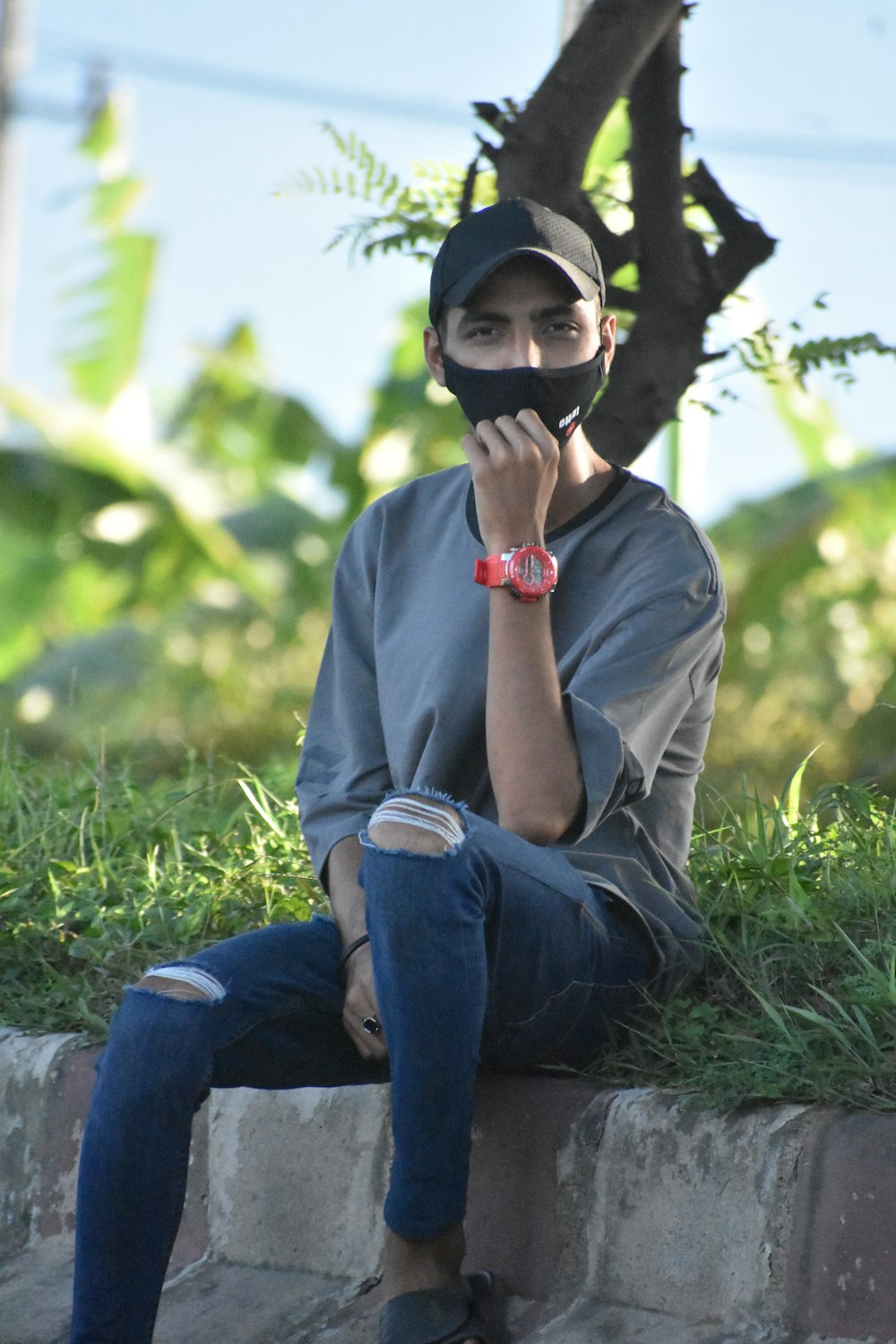 a man sitting on a brick wall with a mask covering his mouth
