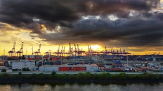 A vibrant port scene at sunset with shipping containers and cranes silhouetted against the sky.